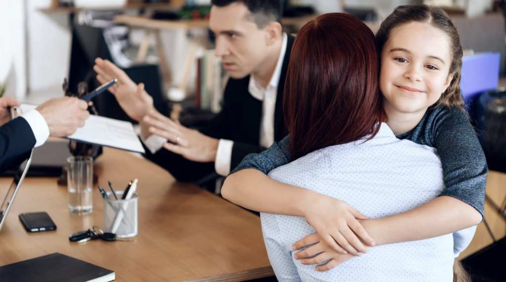 Mujer abrazando a su hija en una oficina, mientras un abogado discute documentos sobre manutenci&oacute;n de hijos en Texas.